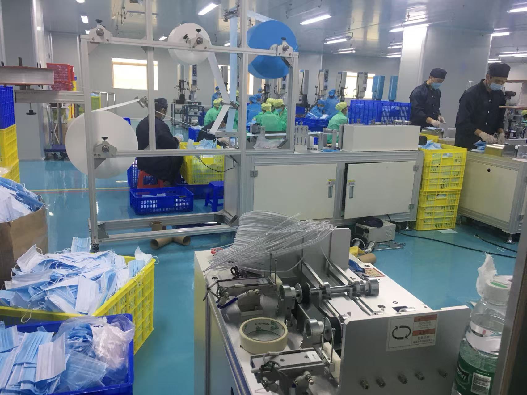 Factory floor view of mask production equipment and material staging