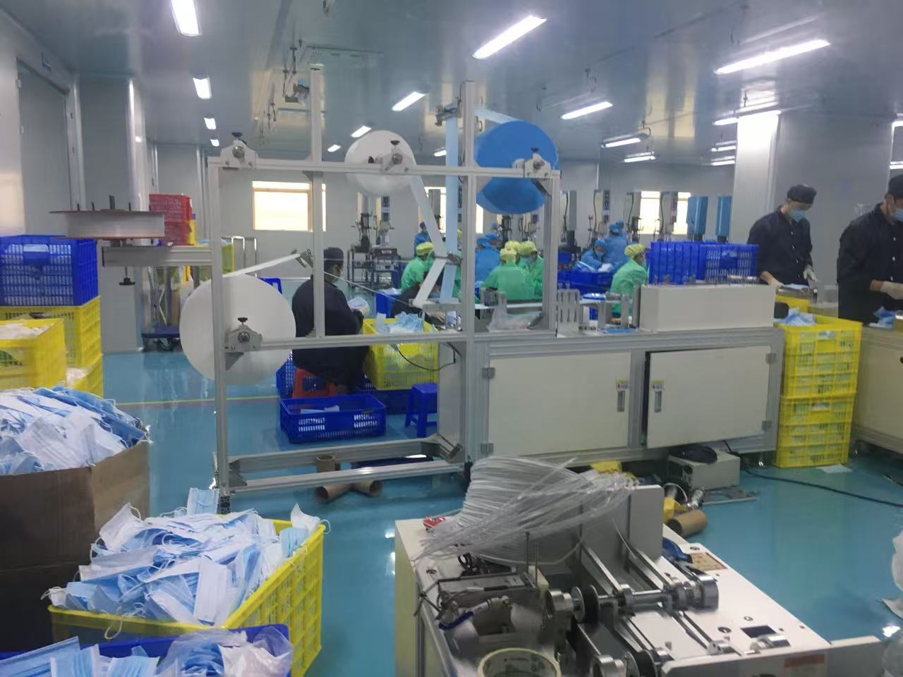 Automated mask-making machinery with raw material rolls on the factory floor